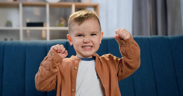 Çağdaş evdeki kanepede oturan yakışıklı, komik çocuk. Yüzünde öfkeyi resmeden ve yumruklarını kameraya dayayan çocuk.