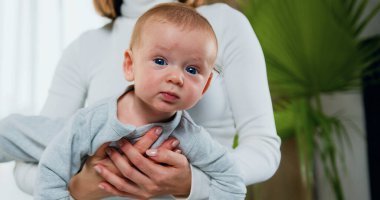 Kollarında gülümseyen bir bebek tutan mutlu bir anne. Sevgi dolu anne yeni doğmuş bebeğini evde taşıyor. Güzel Mutlu Aile. Çocukluk kavramı. Yakın plan..