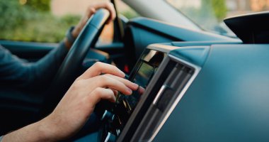 Yakın çekim. Bilinmeyen genç adam kendi lüks sınıfı otomobilinin gidonunun önünde oturuyor ve navigatör kullanıyor..