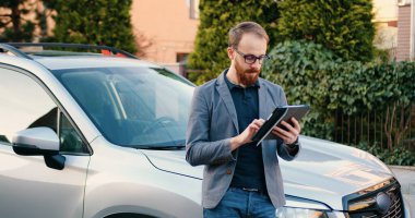 Kahve molası sırasında arabanın yanında dizüstü bilgisayar kullanan beyaz ceketli yakışıklı bir iş adamı..