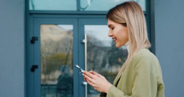 Yakın plan başarılı kadın akıllı telefonuyla sokakta yürüyor ve akıllı telefon kullanarak arkadaşlarıyla sohbet ediyor. İletişim, sosyal ağlar, online alışveriş kavramı.
