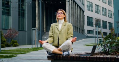 Çekici iş kadını modern ofis binasının yakınında dinleniyor ve meditasyon yapıyor. Yoga yapan güzel kız yorucu bir iş gününden sonra.