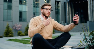 Genç işadamının portresi cep telefonu kullanıyor ve modern bir ofis yakınında konferans konuşması yapıyor..