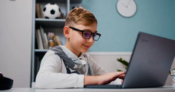 Lachende Schooljongen Bril Met Behulp Van Laptop Zitten Aan Tafel — Stockfoto