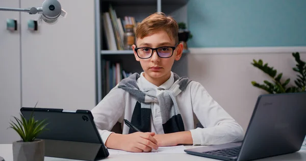 Modern odadaki dizüstü bilgisayarda ödev yapan zeki çocuğun portresi. Kameraya bakıyorum. Ev eğitimi kavramı.