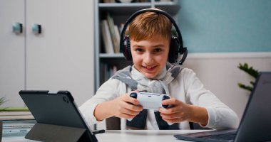 Little boy playing video game on gamepad sitting in living room. Kid dream stay home fun computer addiction. Boy in headphones playing tablet online games.