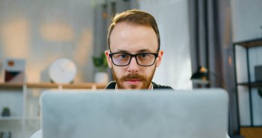 Arkasında gözlüklü ve ev konseptinden uzak, çalışan, çekici, yetenekli, sakallı bir adamın oturduğu bilgisayara bak.