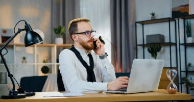 Çekici bir gülümseme. 30 yaşında, evli, sakallı bir ofis çalışanı ev bilgisayarında çalışırken telefonla konuşuyor.