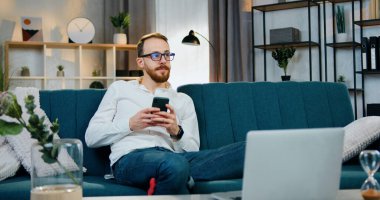 Hayalperest, mutlu, yakışıklı, sakallı, evli bir adam evdeki yumuşak koltukta oturuyor ve karısına akıllı telefondan mesaj yazıyor.