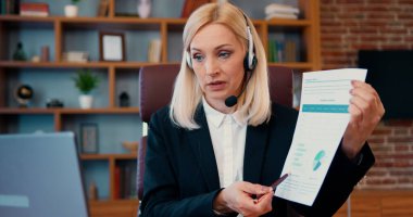 Ofis masasında oturan zarif orta yaşlı iş kadını, bilgisayarında müşteriyle konferans görüşmesi yaptığını gösteriyor.