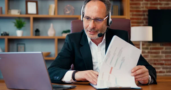 Orta Doğulu patron özgeçmiş kağıdına ve iş görüşmesi görüntülerine bakıyor. İş adamı uzman, takım arkadaşlarıyla çevrimiçi konuşuyor. Belge detaylarını açıkla..