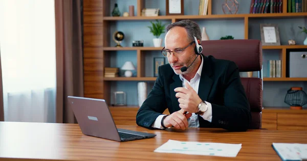 stock image Middle aged business man wearing headset having virtual team meeting on video conference, call using laptop professional training negotiation remote working online in office