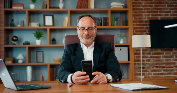 stock image Joyful smiling middle age man chatting use smartphone enjoying break during work in front of laptop