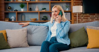 Mutlu orta yaşlı kadın evde tek başına, kanepede dinlenerek, akıllı telefondan konuşarak vakit geçiriyor. Evde sarışın bir kadın telefon görüşmesi yapıyor. Konuşmanın tadını çıkar..