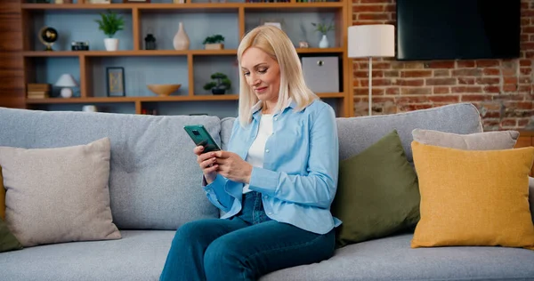 stock image Smiling middle aged lady customer texting mobile sms message playing mobile games using social media apps at home. Millennial woman spending time at home with cell gadget technology.