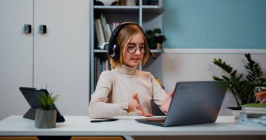 Kafkasyalı akıllı kız kulaklık takıyor, uzaktan kumandalı internet öğretmeniyle konuşuyor sosyal uzaklık video konferansında. Oturma odasındaki bilgisayarda 11 öğrenme sınıfını arıyor.