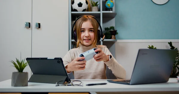 美丽而兴奋的高加索女孩坐在桌旁 用无线控制杆玩电子游戏 — 图库照片