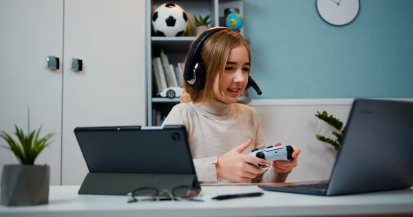 白人10岁的女孩在家里玩电子游戏 快乐的女孩们穿着耳机比赛在家里客厅的笔记本电脑上玩电子游戏 — 图库照片