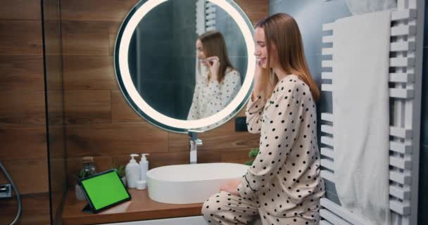 在浴室里微笑着刷牙的年轻女人 美丽的女孩在早上用平板应用程序刷牙时 用美白牙膏刷牙 慢动作 — 图库视频影像