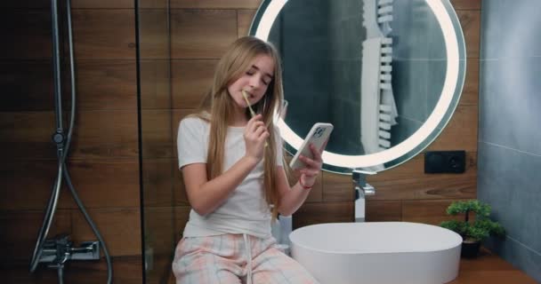 在早上的卫生过程中 用牙刷刷牙 用智能手机在浴室里刷牙 慢动作 — 图库视频影像