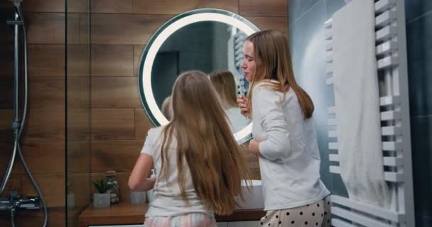 一个穿着长袍的年轻女子站在镜子前 一边跳舞一边刷牙 一边笑着看着对方的浴室 慢动作 — 图库视频影像