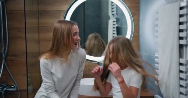 两个有趣的白人女孩 有着美丽的长发 在家里的现代浴室里和吹风机一起跳舞唱歌 慢动作 — 图库视频影像