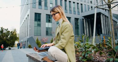 Kampüs çimlerinde otururken dizüstü bilgisayar kullanarak çalışan ya da ders çalışan çekici beyaz kadın. Güzel kız öğrenci açık hava derslerine hazırlanıyor.