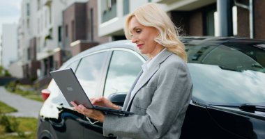 Modern arabaları arka sokaktayken iş kadını dizüstü bilgisayarda çalışıyor.