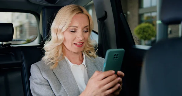 stock image Professional business woman writing message and chatting on smartphone in modern car. Beautiful lady is commuting from office in a backseat of her car.