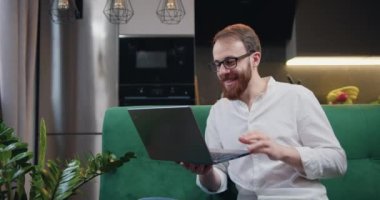 Kablosuz gözlüklü çekici genç adam evde video görüşmesi yapıyor. Oturma odasında kanepede oturmuş sohbet eden bir erkek. Yavaş çekim.
