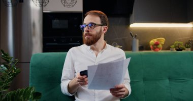 Mutfaktaki kanepede oturan hesap makinesini kullanarak mali işlerle ilgilenen bir adam. Finansal konsept. Evde veri analiz eden odaklanmış bir adam.