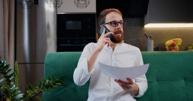 Uzak bir iş yerinde belgelerle çalışan bir adam. İş adamı cep telefonundan konuşuyor ve evdeki mali belgeleri gözden geçiriyor..