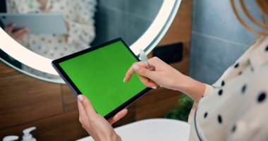 Evdeki banyoda yeşil ekranlı siyah tablet kullanan kadın ellerinin yakın çekimi. Arkadan bak. Krom anahtar