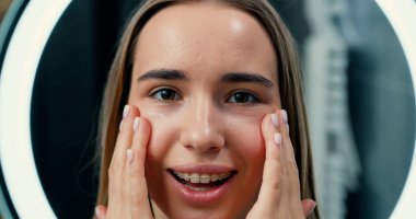 Gülen kızın yüzüne nemlendirici krem sürmesine yakın. Banyo arka planında kusursuz cildi olan güzel bir kızın portresi. Cilt bakımı ve güzellik kavramı