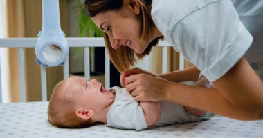 Genç ve güzel bir anne beşiğindeki küçük bebeğe gülümsüyor. - Yakın çekim. Sevimli küçük bebek, ebeveyn ilgisinin yatakta uzanmasından hoşlanıyor..