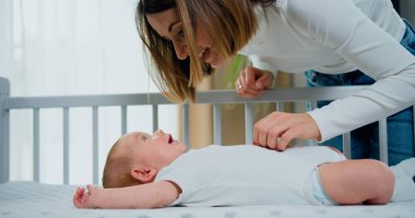 Yakından bir portre. Güzel anne beşikteki sevimli bebeği oynatıyor ve sakinleştiriyor. Gülümseyen bir anne ve küçük sevimli bir bebek. Mutlu aile kavramı.