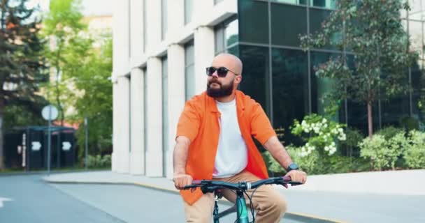 街の通りに自転車に乗ってサングラスをかけた若い髭のヒップスター男が仕事に行く 都市旅行の概念 ハンサムなひげそりのマネージャーは自転車で働くために成功したCeo通勤 スローモーション — ストック動画