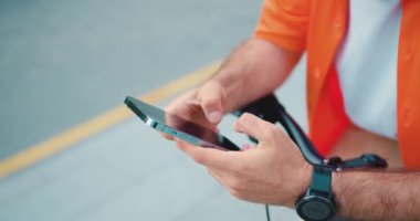 Erkek eller cep telefonunu tutsun. Tanımlanamayan erkek bisikletçi bir mesaj yazarken ve bisikletin yanında dururken akıllı telefon kullanır. Yavaş çekim.