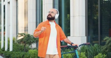 Hippi bir banliyö sakini sokakta bisikletiyle kulaklıkla yürürken ve akıllı telefonunda müzik dinleyip dans ederken. Bisikletin üzerinde dinlenirken şarkının tadını çıkarıyorum. Yavaş çekim.