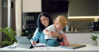 Modern, genç bir anne, küçük oğlunu kucağında tutuyor, evinde dizüstü bilgisayar kullanıyor. Annem evde çalışıyor, online alışveriş yapıyor, sosyal medya izliyor ya da e-posta yazıyor. Yavaş çekim.