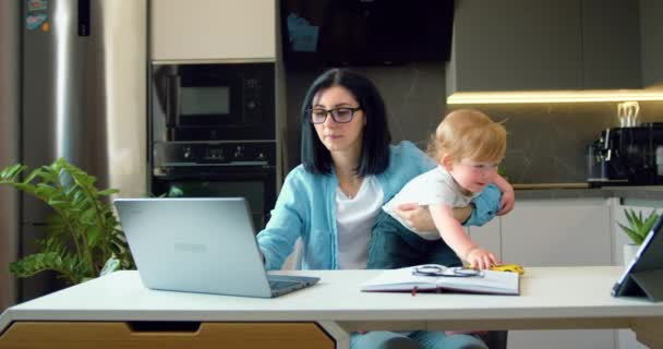 Mujer Con Hijo Pequeño Sienta Casa Mesa Trabaja Ordenador Portátil — Vídeos de Stock