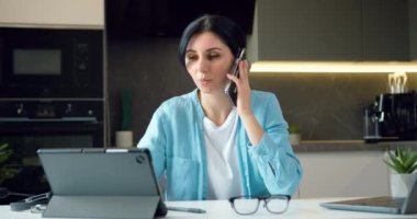 Müşteri danışmanlığı için dijital tablet kullanan, gülümseyen, gülen ve ofisteki iş arkadaşıyla telefon görüşmesi yapan güzel bir kadın. Yavaş çekim.