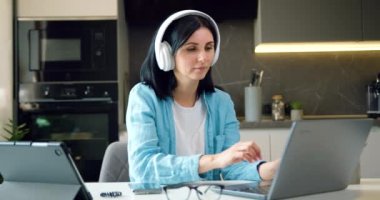 İş kadını kablosuz kulaklıklar evde dizüstü bilgisayar kullanarak internette gezinen ve sosyal medyayı yöneten genç bir kadın. E-hocayla öğren, bilgiyi geliştir video kullan, modern teknoloji