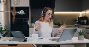 Kulaklıklı genç beyaz kadın internet konferansında müşteriyle video çağrı merkezi operatörü aracılığıyla iletişim kuruyor. Yavaş çekim