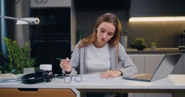 Masada oturan bayan pazarlama müdürü mutfak arka planındaki ofiste finansal ve pazarlama belgeleriyle çalışıyor. Yavaş çekim