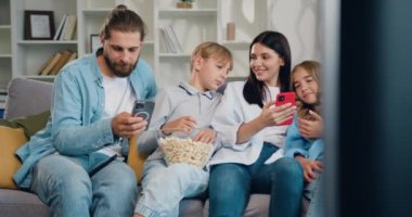 Dört kişilik mutlu bir aile akıllı telefon teknolojisi kullanmaktan keyif alır. Kanepede oturup akıllı telefon tutarak sohbet eden arkadaşlarınızı görmezden gelin. Yavaş çekim.