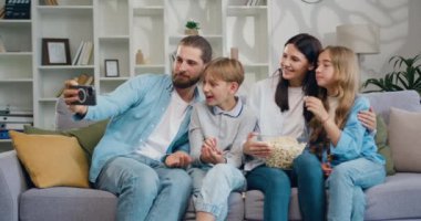 Güzel gülümseyen bir aile akıllı telefon kamerasında özçekim fotoğrafları çeker. Neşeli kız oğlan, telefonda komik fotoğraflar çeken ebeveynler. Hafta sonu eğleniyor ve dinleniyoruz. Yavaş çekim.