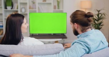 Çift evdeki kanepede birlikte oturuyor, kroma tuşlu yeşil ekranlı TV programları izliyorlar. Karı koca evde birlikte dinleniyor. Yeşil ekran. Kromakey. Ev sineması. Yavaş çekim.
