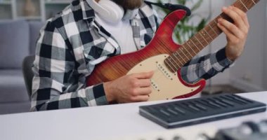Kafkas sakallı, kulaklıklı, evde elektronik gitar dersi alan ve dizüstü bilgisayarı olan genç bir adamı yakın çekim. Yavaş çekim