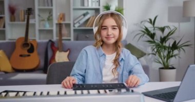 Çocuk yaşta müzik aleti çalmayı öğrenen ve kameraya bakan bir kızın portresi. Oturma odasında ya da müzik okulunda kulaklıkla piyano çalan güzel bir kız çocuğu. Yavaş çekim